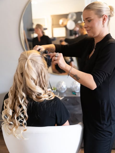 Nikki krult lang blond haar in de witte knipstoel, ronde spiegel